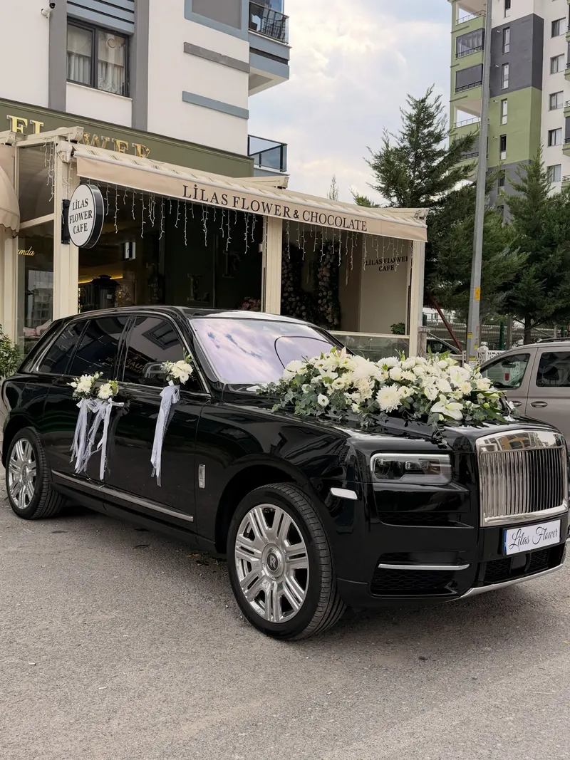 LİLAS FLOWER & CHOCOLATE tenteli dükkânın önünde kaputu ve kapıları beyaz çiçeklerle süslenmiş siyah gelin arabası
